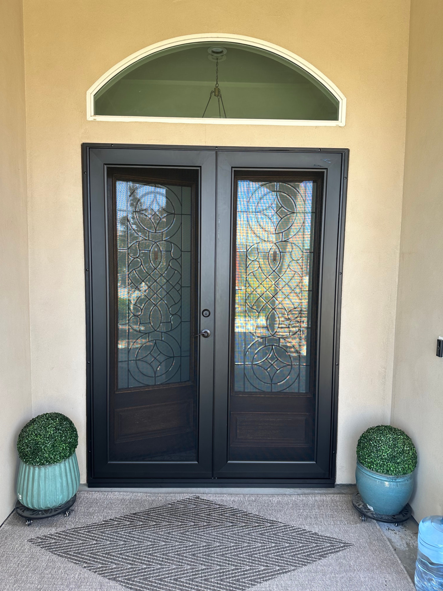 Large dark double security doors with decorative glass-like patterns under an arched transom